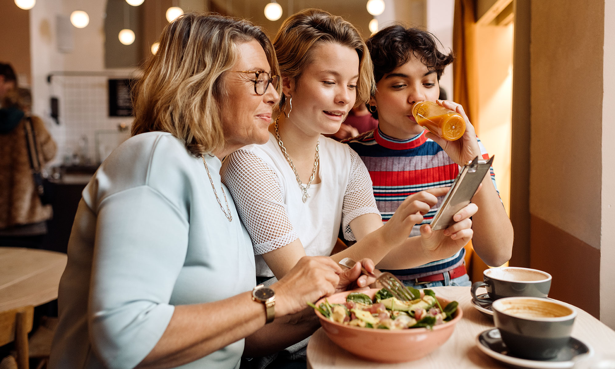 Tre kvinnor sitter och äter lunch på ett café och tittar på en mobiltelefon