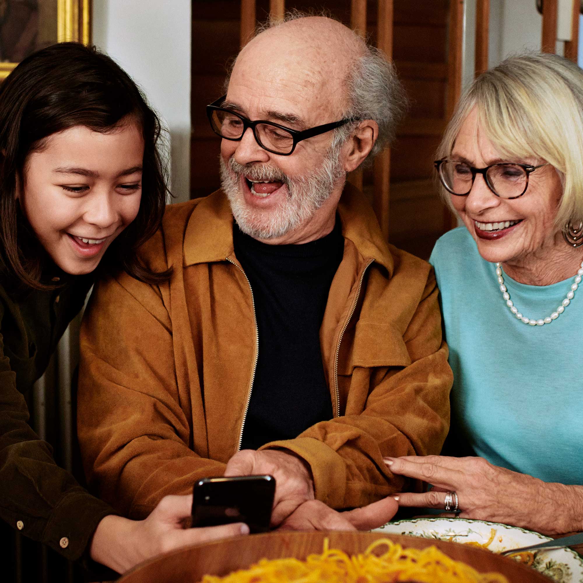 Ett äldre par och en ungdom tittar på en mobil och skrattar